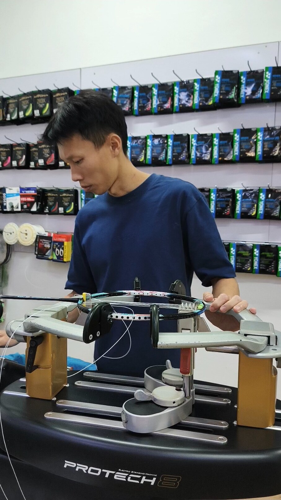 Koh Jian Long Kelvin operating the stringing setup with the badminton racquet secured in its supports Koh Jian Long Kelvin operating the stringing setup with the badminton racquet secured in its supports