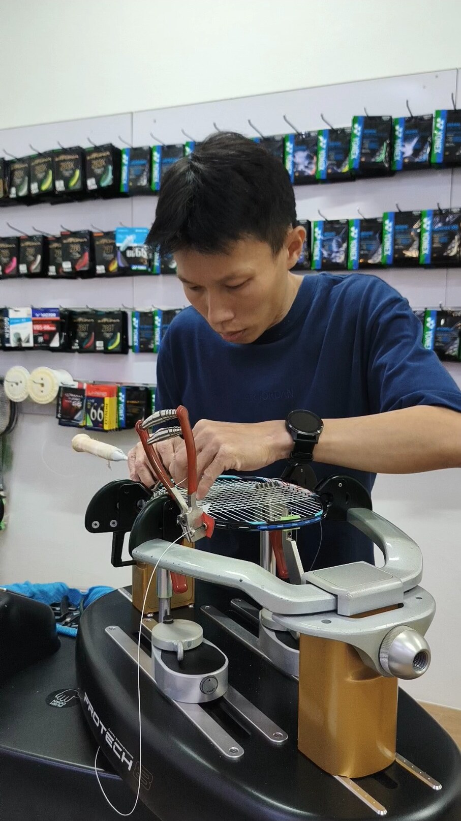 Koh Jian Long Kelvin working carefully at the badminton racquet's tie-off area with a starting clamp beside the frame Koh Jian Long Kelvin working carefully at the badminton racquet's tie-off area with a starting clamp beside the frame