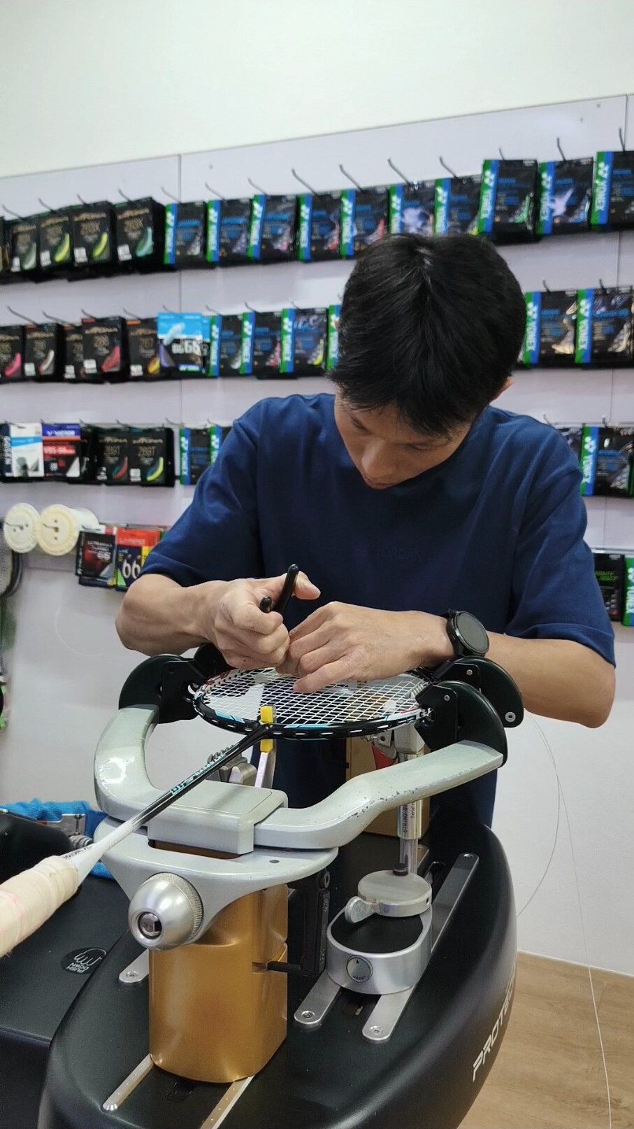 Koh Jian Long Kelvin using a hand tool at the racquet frame while finishing a badminton stringing task Koh Jian Long Kelvin using a hand tool at the racquet frame while finishing a badminton stringing task