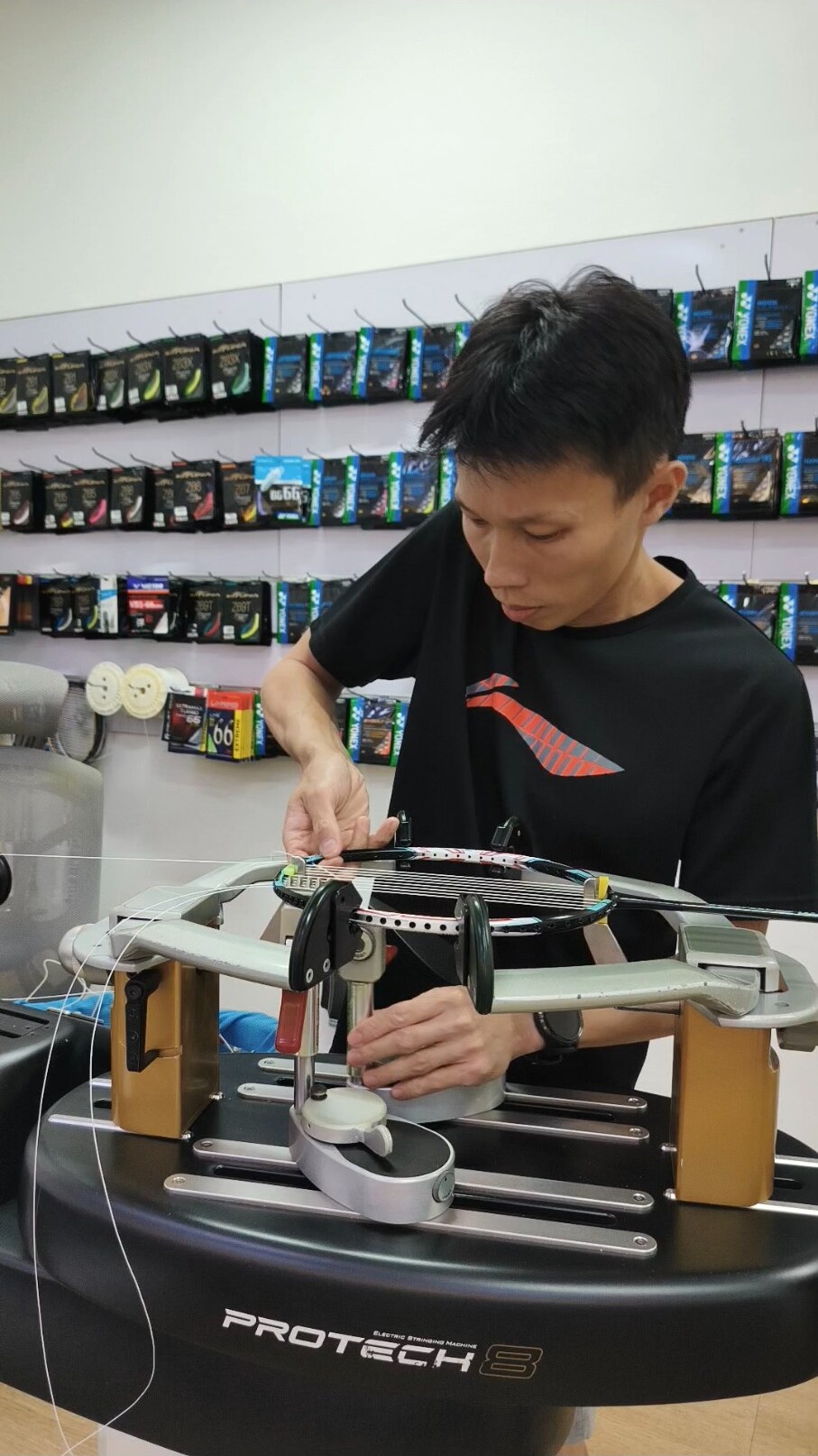 Koh Jian Long Kelvin guiding string near the badminton racquet frame while adjusting the clamp base Koh Jian Long Kelvin guiding string near the badminton racquet frame while adjusting the clamp base