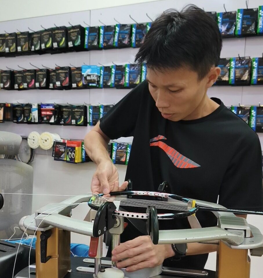 Koh Jian Long Kelvin guiding badminton string and adjusting the clamp at the stringing machine Koh Jian Long Kelvin guiding badminton string and adjusting the clamp at the stringing machine
