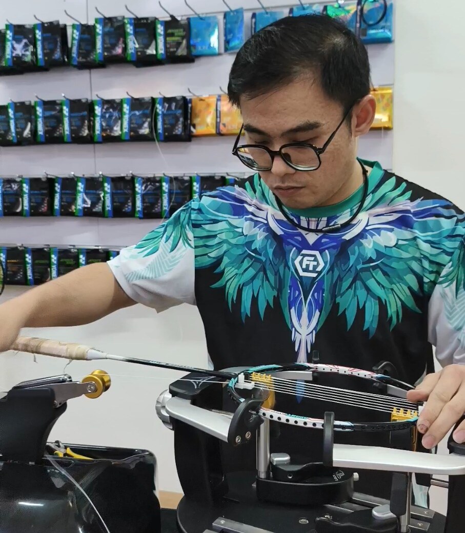 Ng Kim Way working beside the tensioning unit with a badminton racquet secured on the stringing machine Ng Kim Way working beside the tensioning unit with a badminton racquet secured on the stringing machine