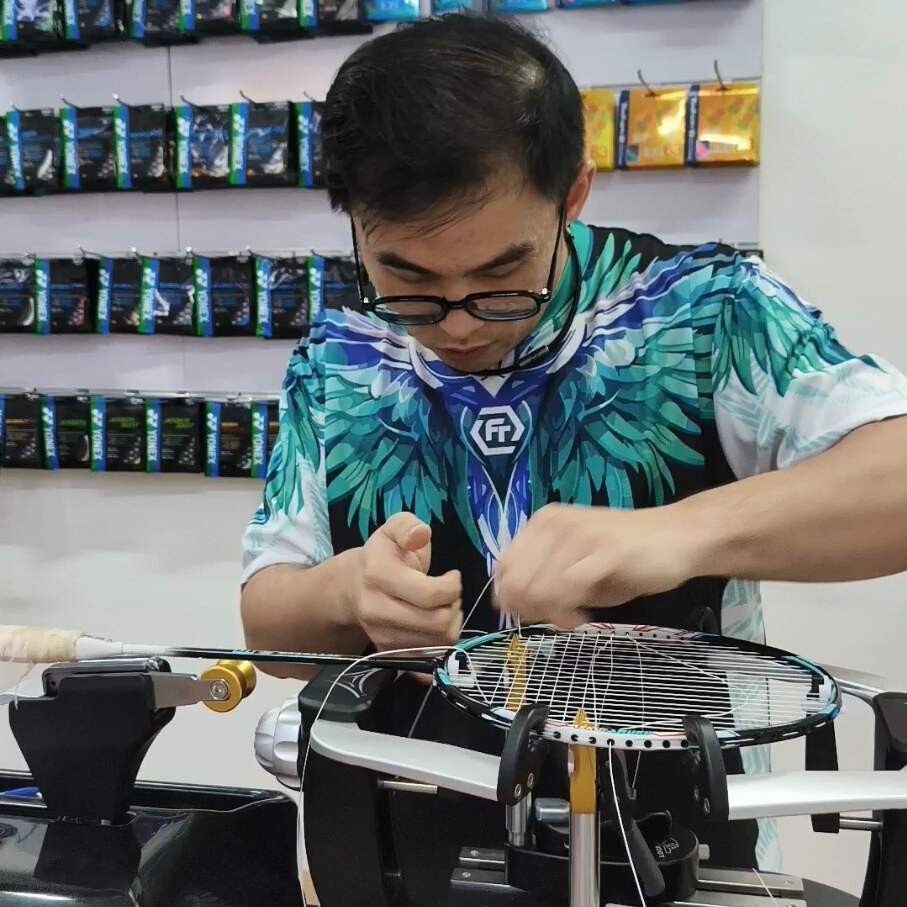 Ng Kim Way handling string with both hands over a mounted badminton racquet